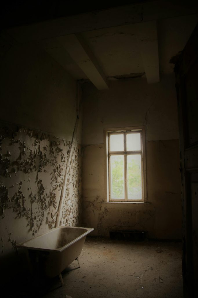 Interior of abandoned room with shabby walls and old bathtub placed in front of window